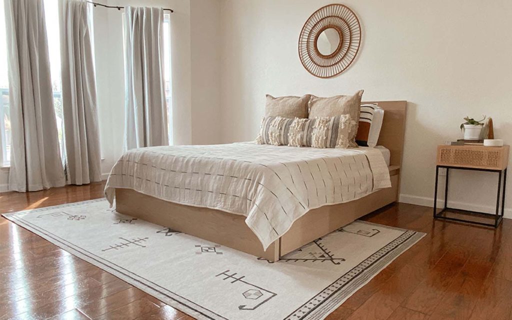Neutral rug placed under a bed with soft, neutral decor in a minimalist bedroom
